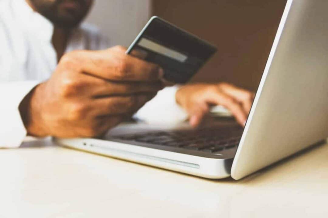 Pessoa usando computador com cartão de crédito na mão