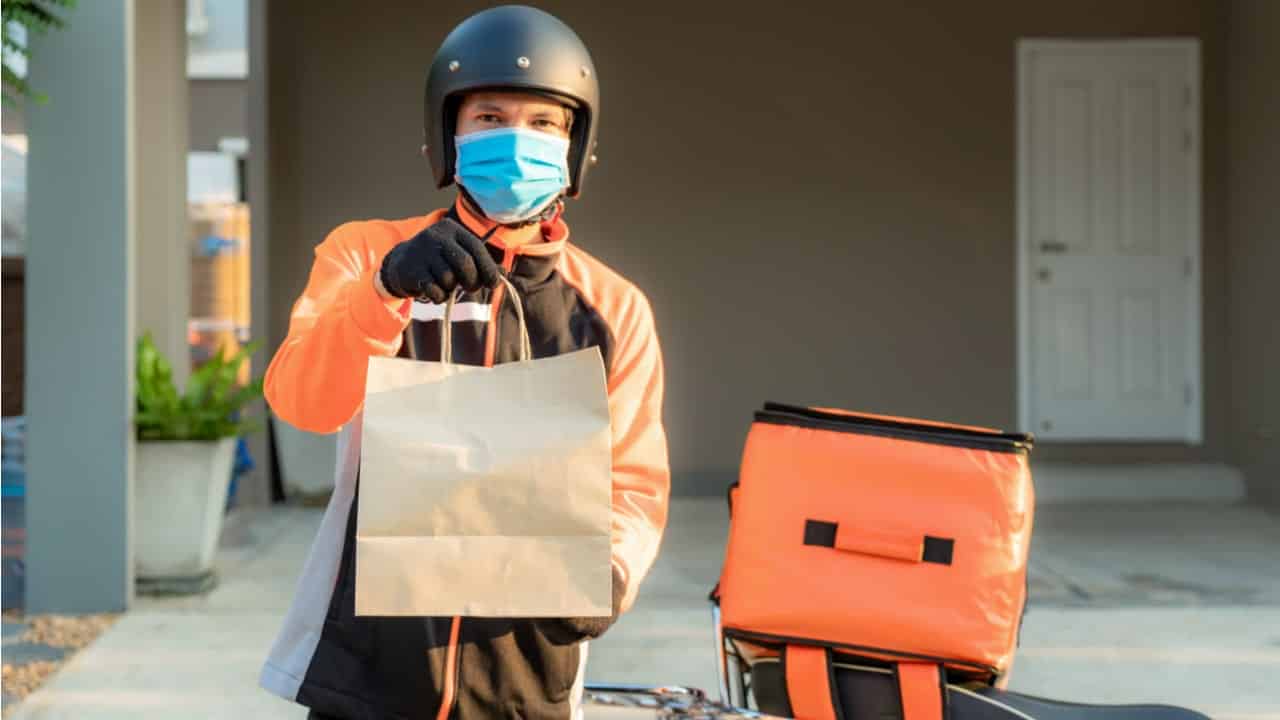Entregador de delivery ao lado de sua moto, segurando uma sacola com algum produto.