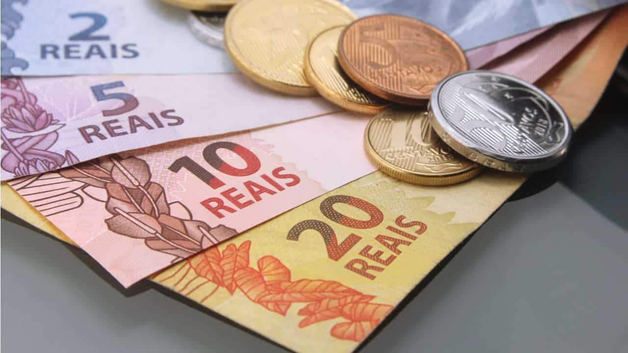 Notas de real sob moedas em uma superfície cinza