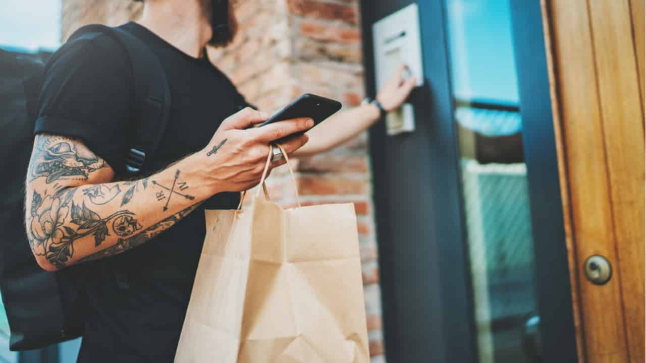 entregador faz entrega de compra delivery em frente a porta enquanto segura celular