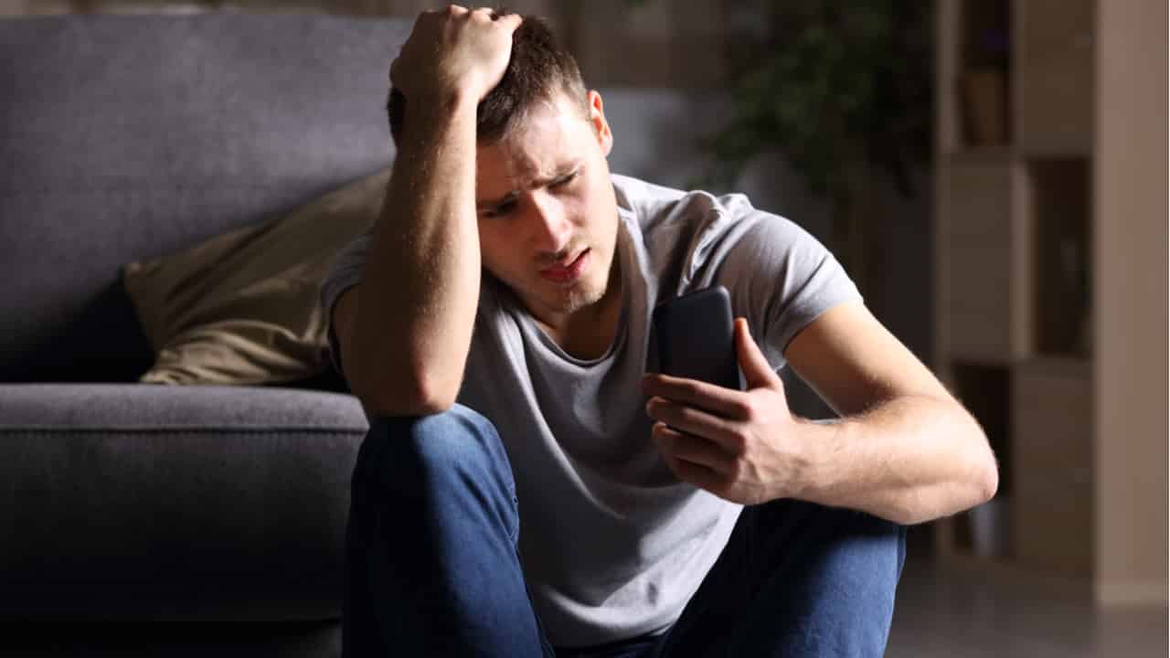 Homem preocupado sentado no chão olhando para aparelho celular