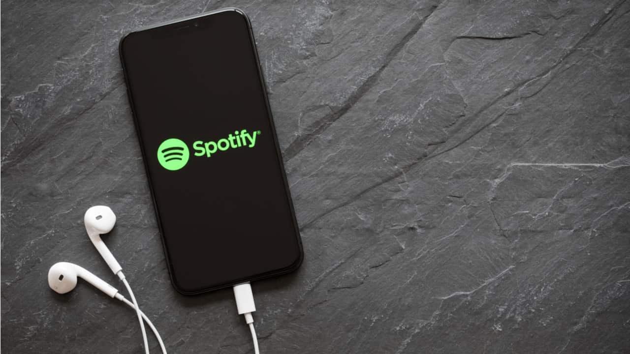 Celular sobre uma superfície com aplicativo do Spotify aberto e fone de ouvido conectado