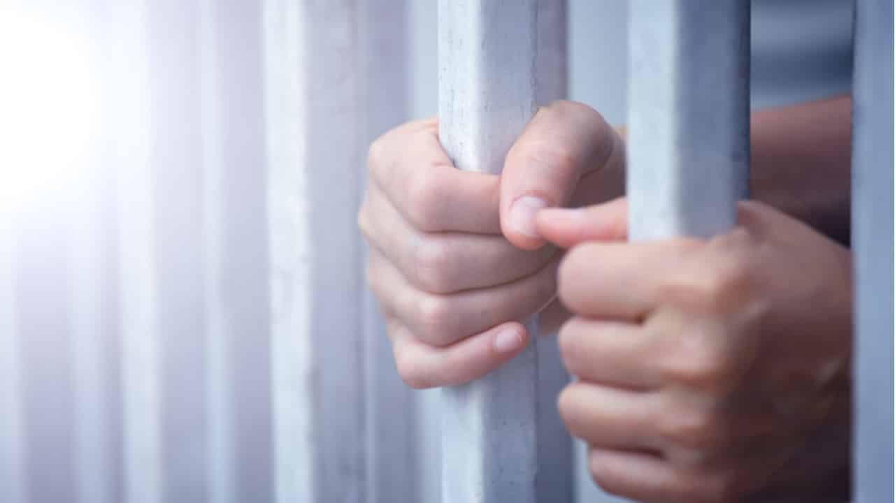 homem preso atrás das grades de detenção, suas mãos seguram nas grades