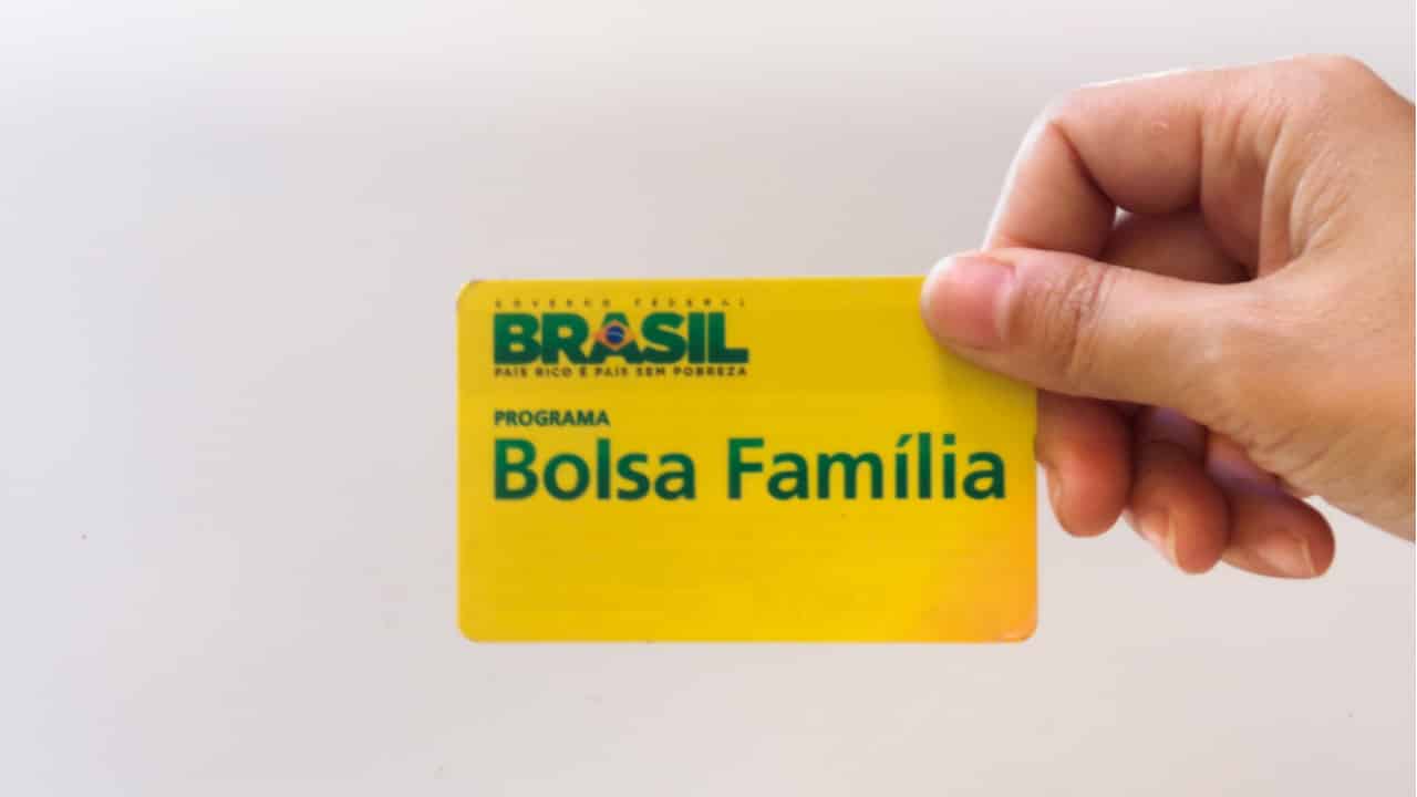 imagem de uma mão de pessoa branca segurando um cartão amarelo do Bolsa Família