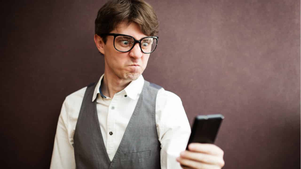 Rapaz olha com cara engraçada para o telefone na mão