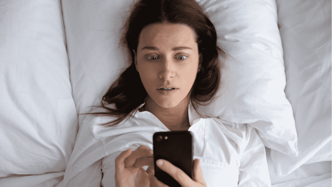 mulher deitada olha chocada para celular