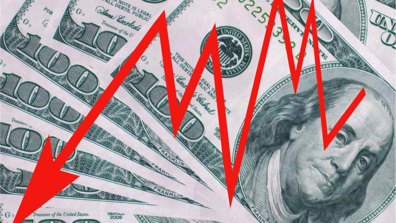 Imagem de notas de dólar com uma seta vermelha em zigue-zague vertical sobre a imagem, representando a queda do dólar