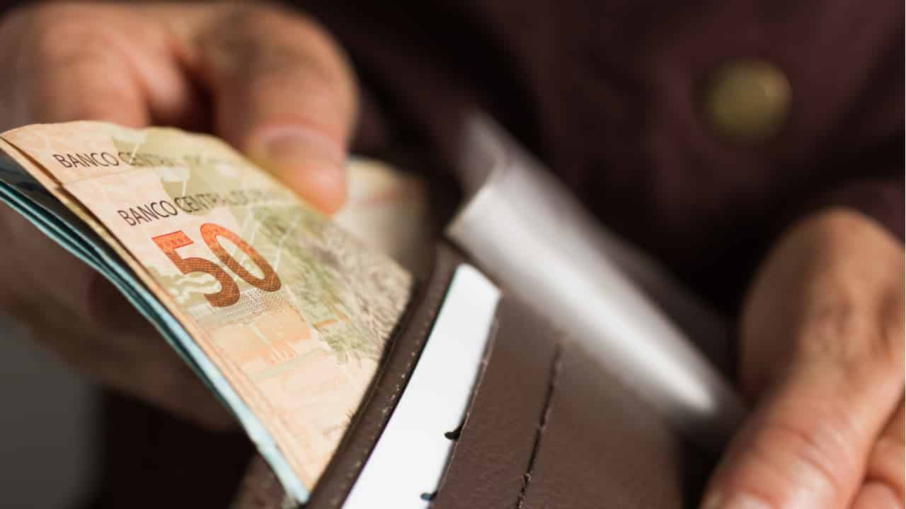 Notas de real sendo postas em uma carteira