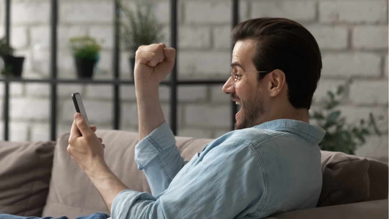 Homem branco comemorando enquanto olha para o seu celular