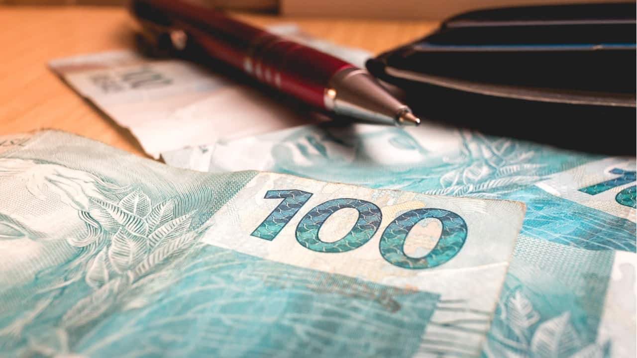 Duas cédulas de 100 reais com uma caneta em cima.