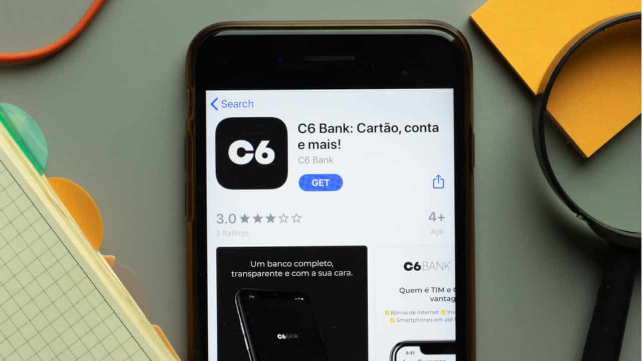 Celular com app da C6 Store sobre uma mesa