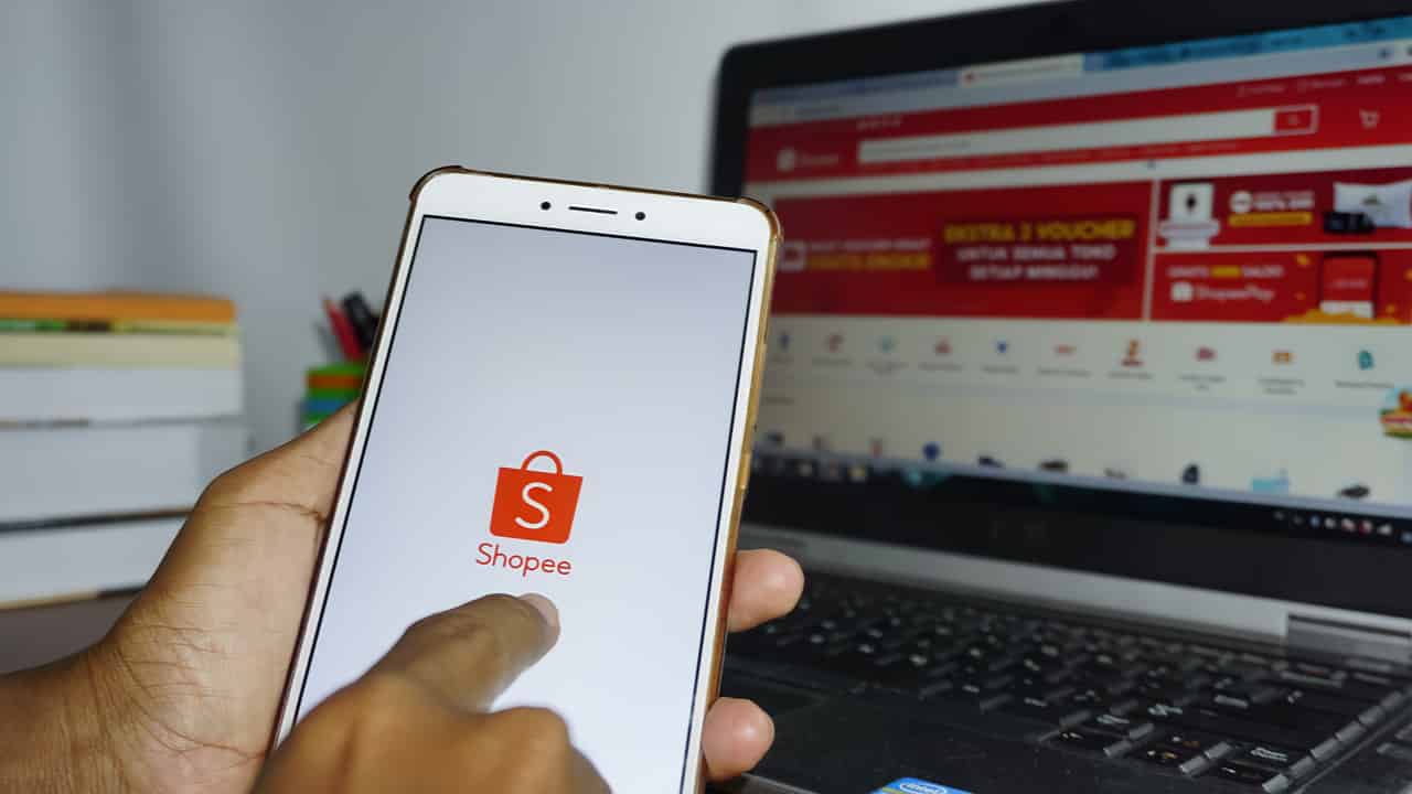Celular com app da Shopee aberto e, ao fundo, computador com site da Shopee
