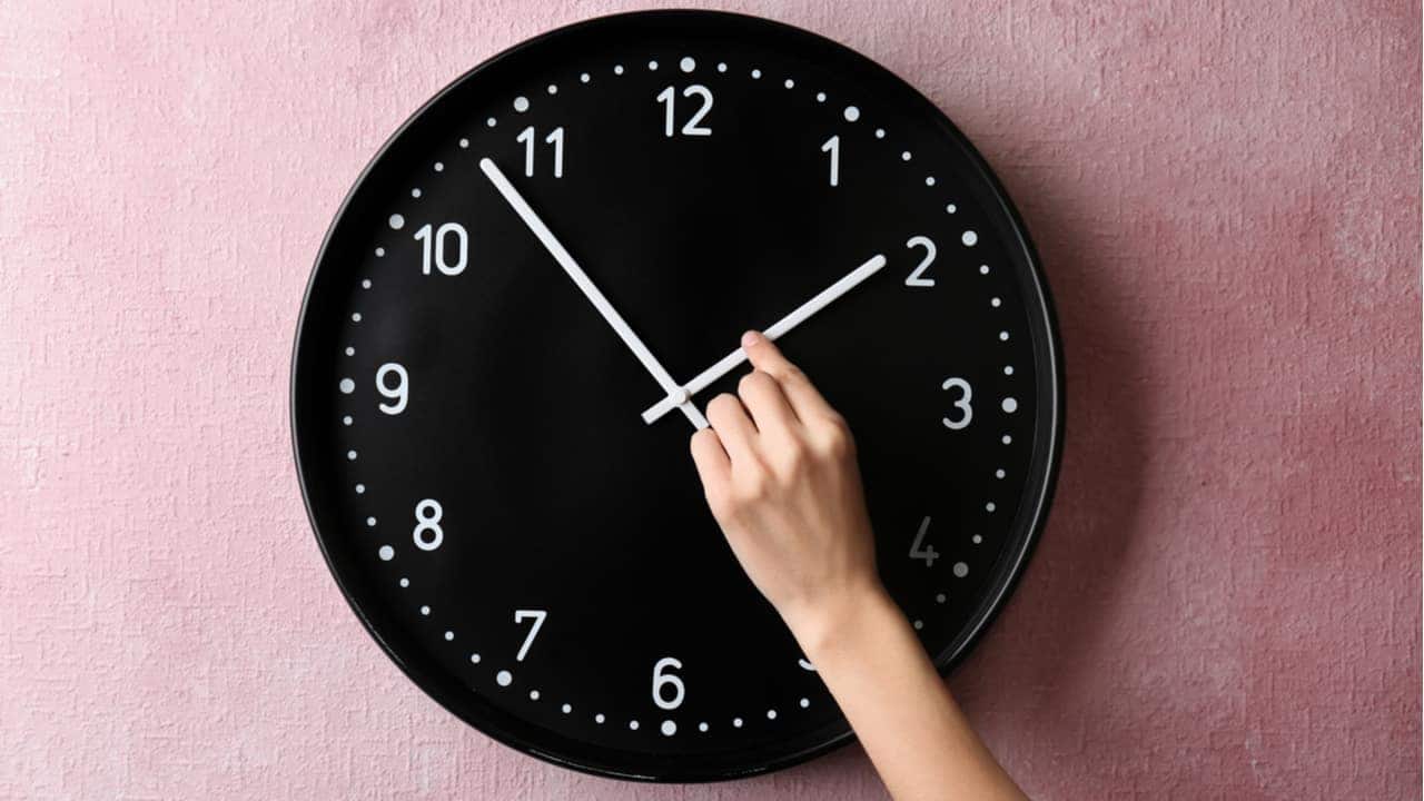 A imagem mostra um relógio de parede, preto, tendo os ponteiros alterados.