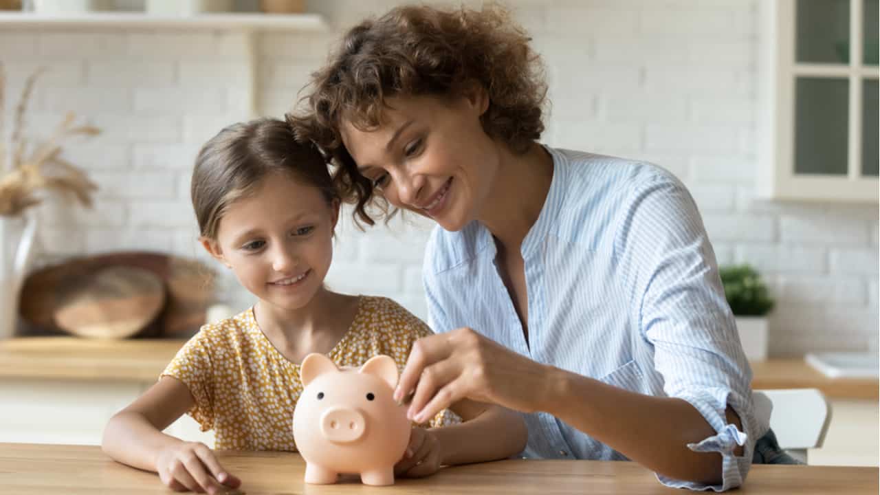 Mãe e filha depositando dinheiro em um cofrinho