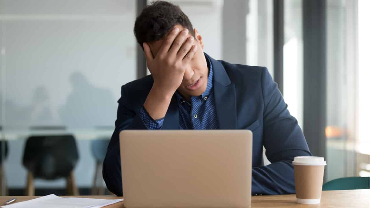 a imagem mostra um homem na frente de um notebook com as mãos sobre o rosto.