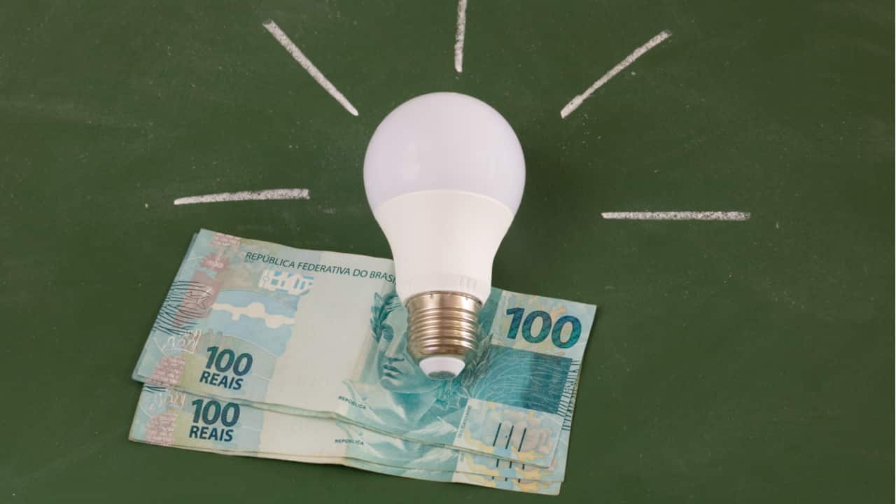imagem de lâmpada acessa e ao fundo notas de 100 reais