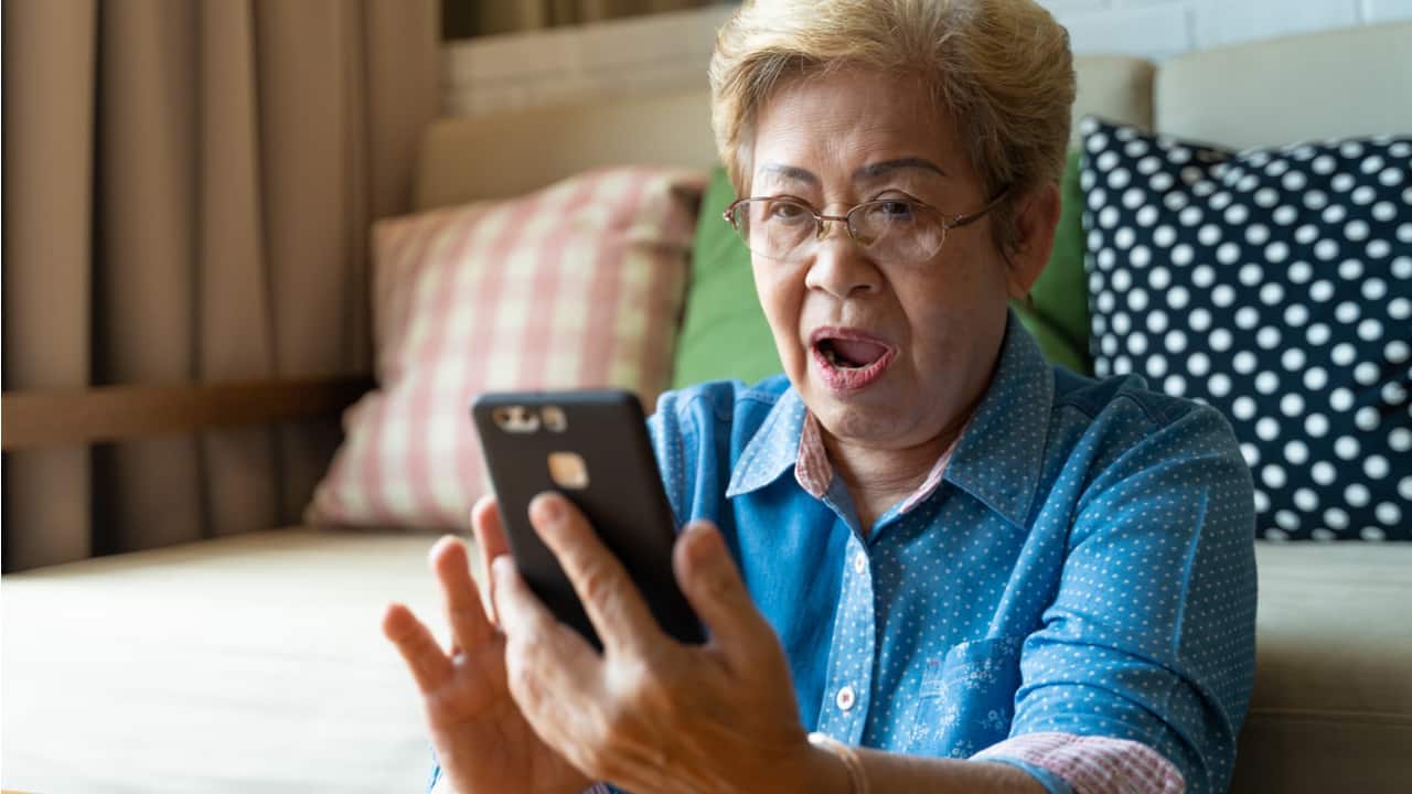 Senhora olhando para seu celular com feição de espanto ao ver que é possível desistir da aposentadoria do INSS