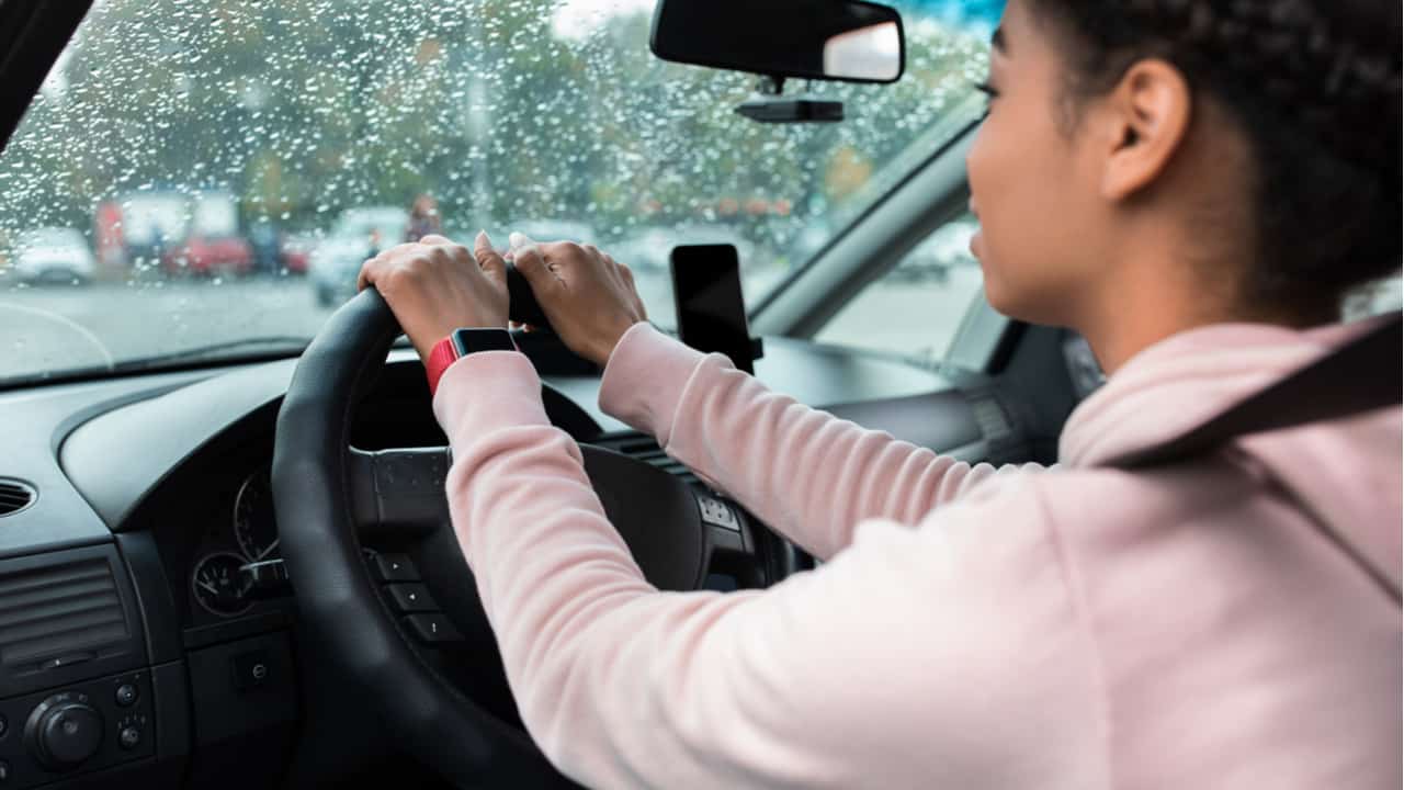 Motorista com as mãos ao volante dirigindo em dia de chuva seguro