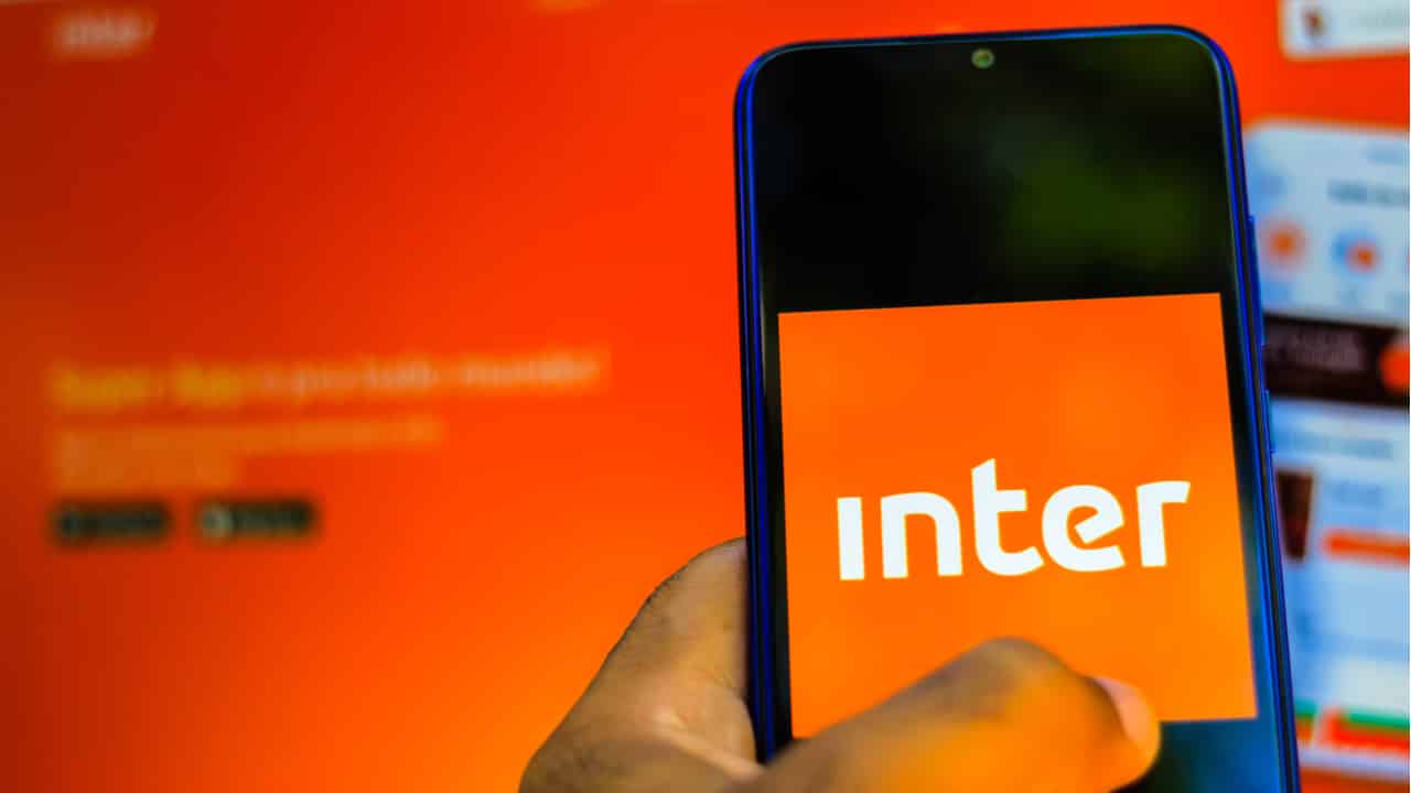 Celular com o app do Inter aberto e ao fundo o site, em laranja.