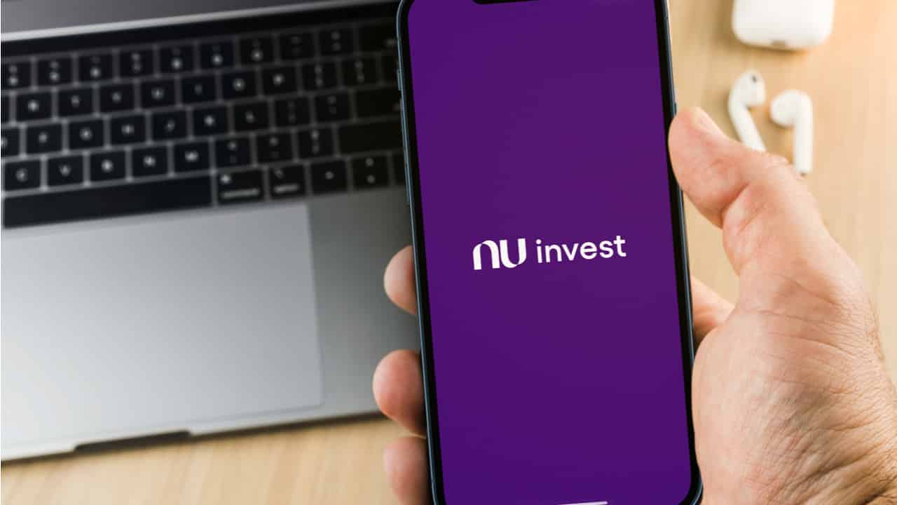 Imagem de aplicativo do Nu invest no celular, com notebook ao fundo