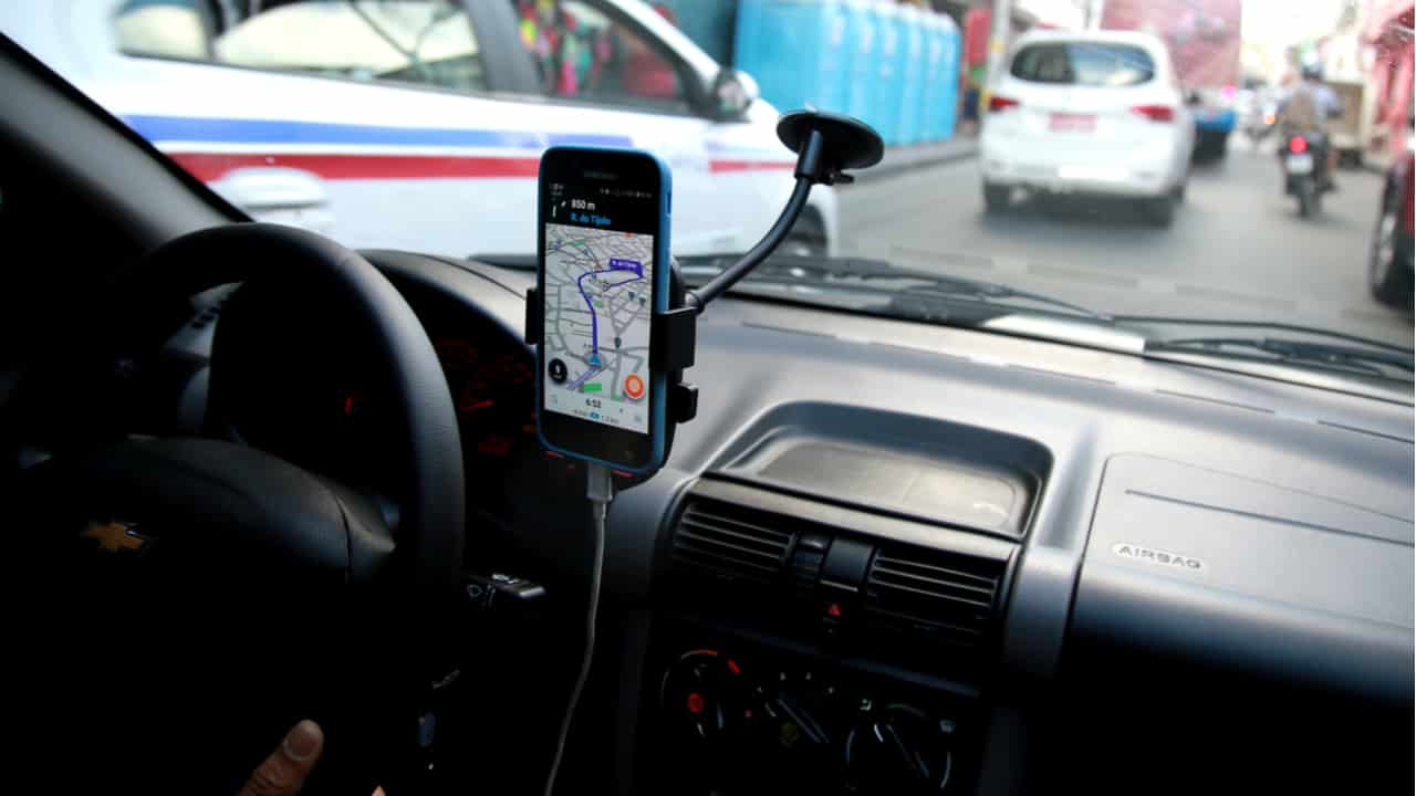 imagem de dentrod e um carro com aplicativo de localização conectado na tela do celular acoplado ao painel do carro