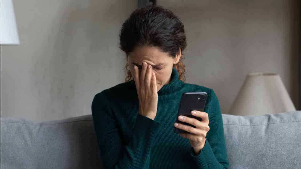 mulher preocupada com a mão no rosto e segurando o celular