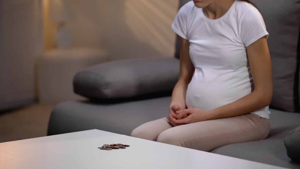 Uma gestante sentada em um sofá com as mãos apoiadas no colo