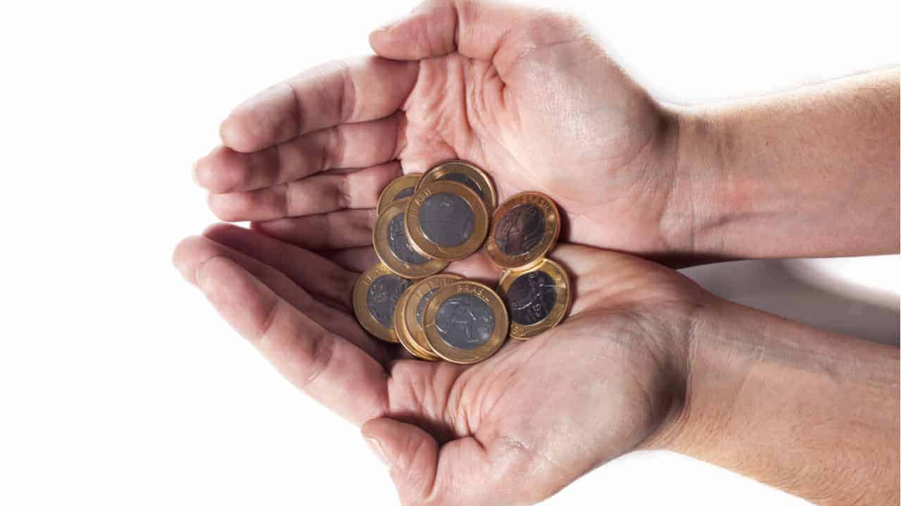 Mãos segurando moedas de 1 real