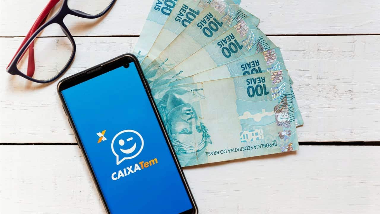 celular com aplicativo da Caixa Tem e cédulas de dinheiro