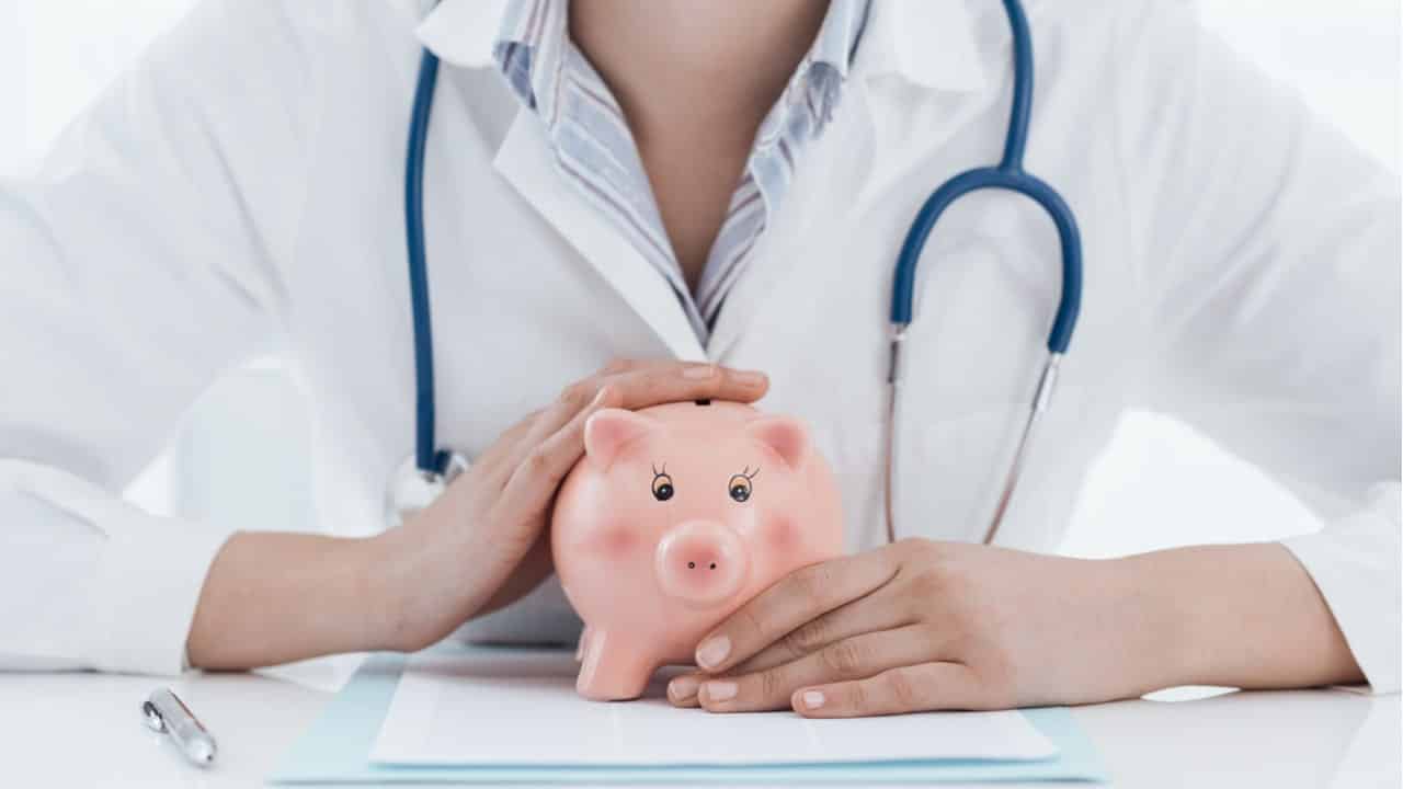 Médica com um estetoscópio, enquanto segura um cofre de porquinho, que faz alusão à economia. planos de saúde