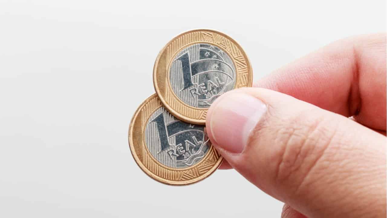 Pessoa segurando 2 moedas de 1 real