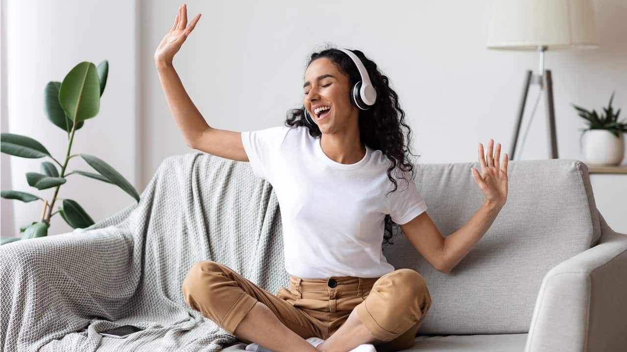 Mulher feliz ouvindo música sentada no sofá de pernas cruzadas e balançando os braços. amazon music