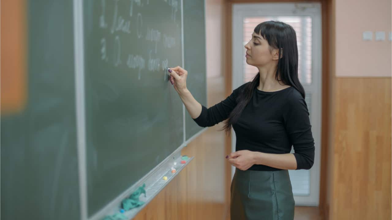 Professora escrevendo em quadro negro na sala de aula