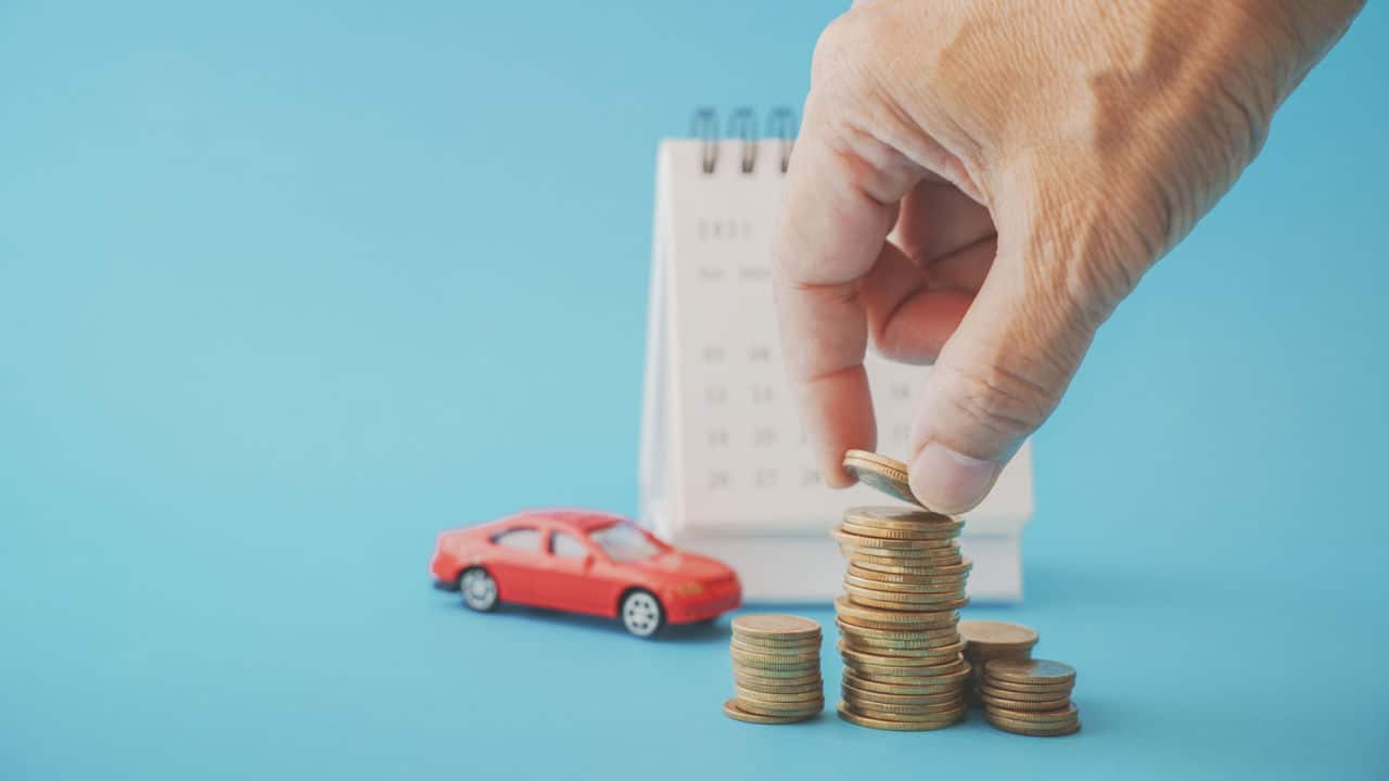 Miniatura de carro e homem empilhando moedas ao lado de um bloco de notas