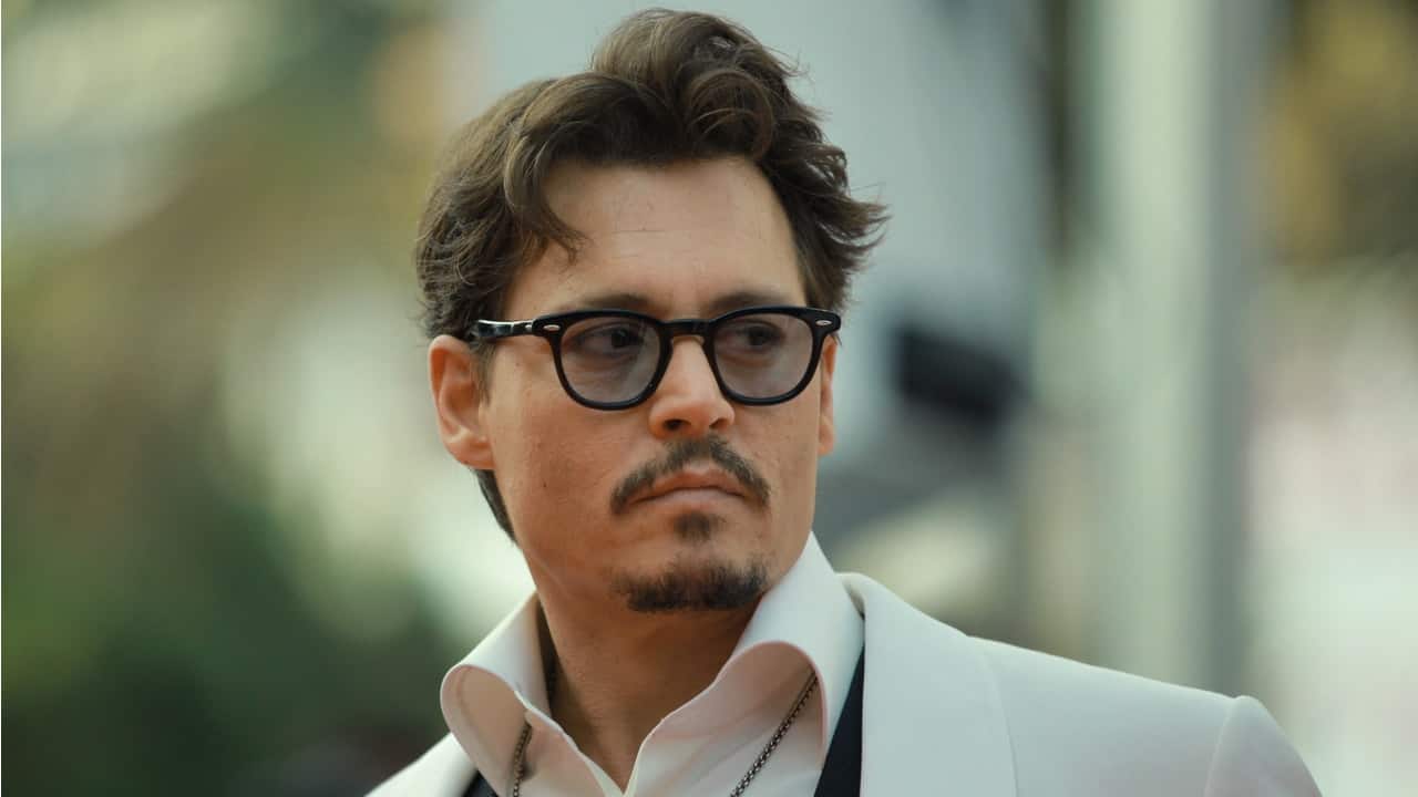 o ator norte-americano Johnny Depp usando óculos e blazer branco, durante evento com a imprensa