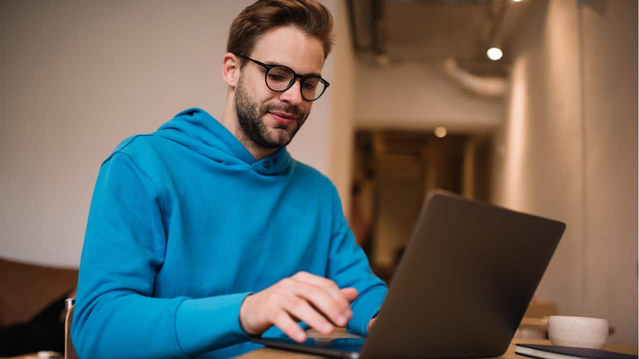 Homem usando casaco azul sentado utilizando um notebook