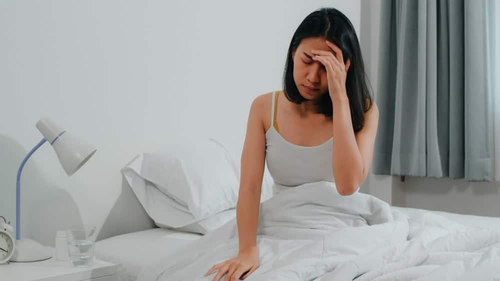 Mulher sentada na cama com dor de cabeça
