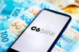 Celular com o logo do C6 Bank sobre notas de dinheiro