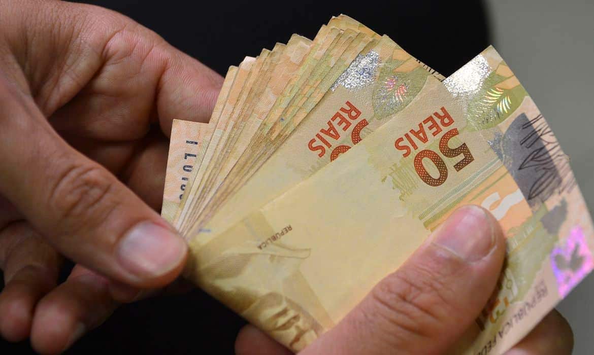 Mão segurando notas de R$ 50,00