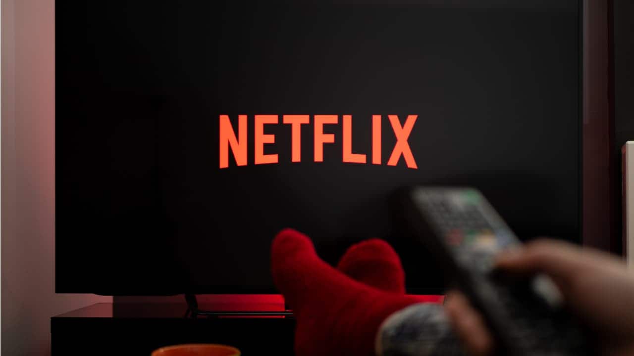 Uma mão aponta um controle remoto para uma TV com o logo da Netflix