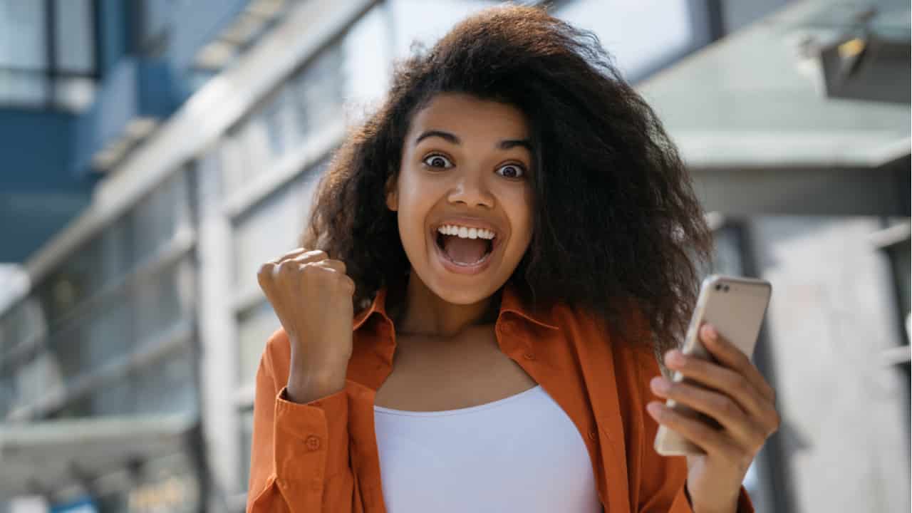 Imagem de jovem negra eufórica de felicidade com celular na mão