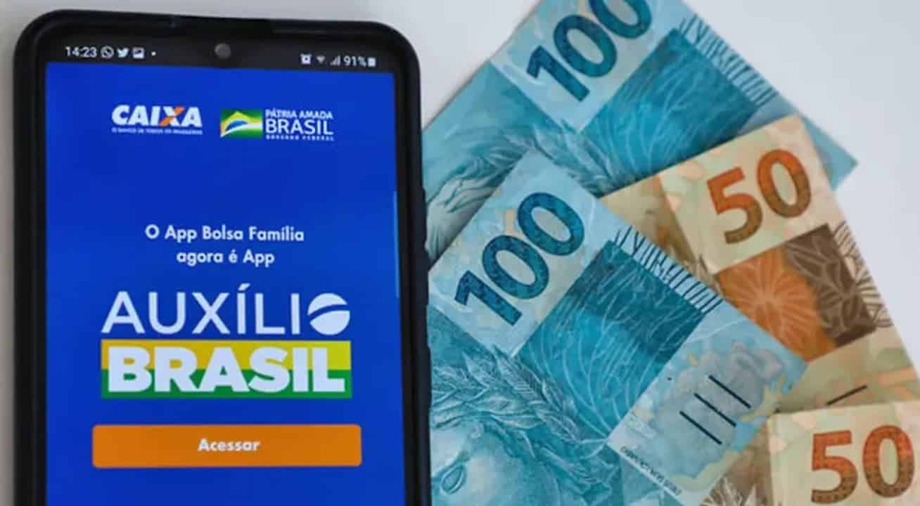 Celular com tela do Auxílio Brasil. Duas notas de cem reais e duas de cinquenta