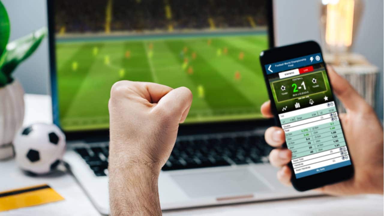Torcedor assistindo a jogo pelo computador enquanto comemora resultado de bolão no celular