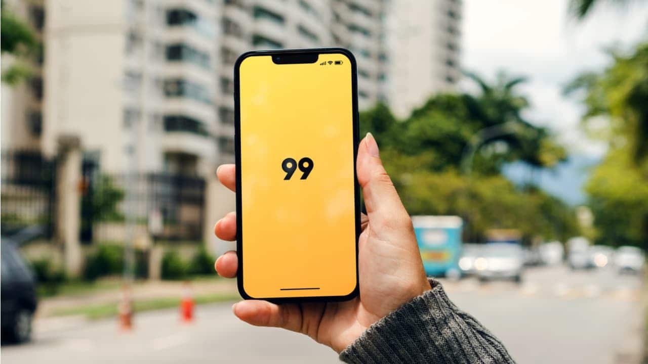 Mão segurando celular com tela exibindo o aplicativo 99