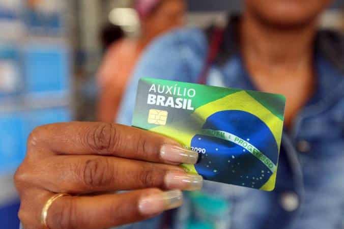 Mão feminina segurando um cartão do Auxílio Brasil