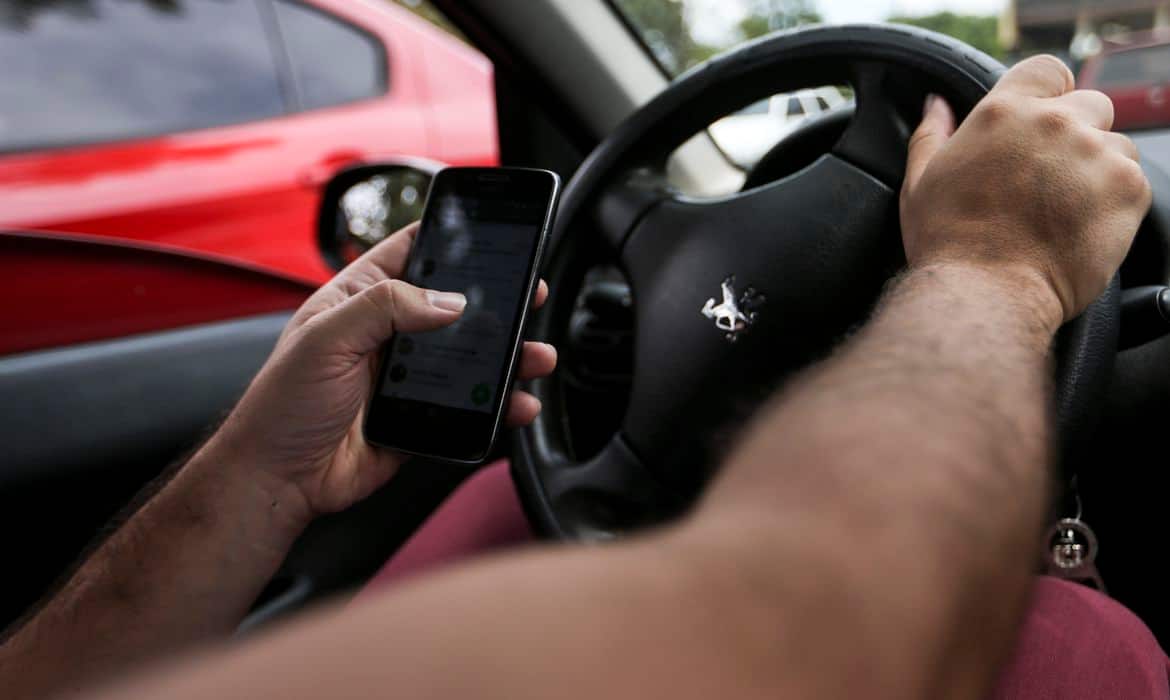 Motorista dirigindo com celular na mão trabalhadores