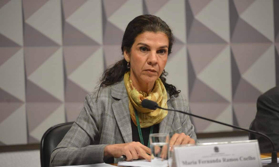Mulher branca de cabelos ondulados e castanhos falando ao microfone