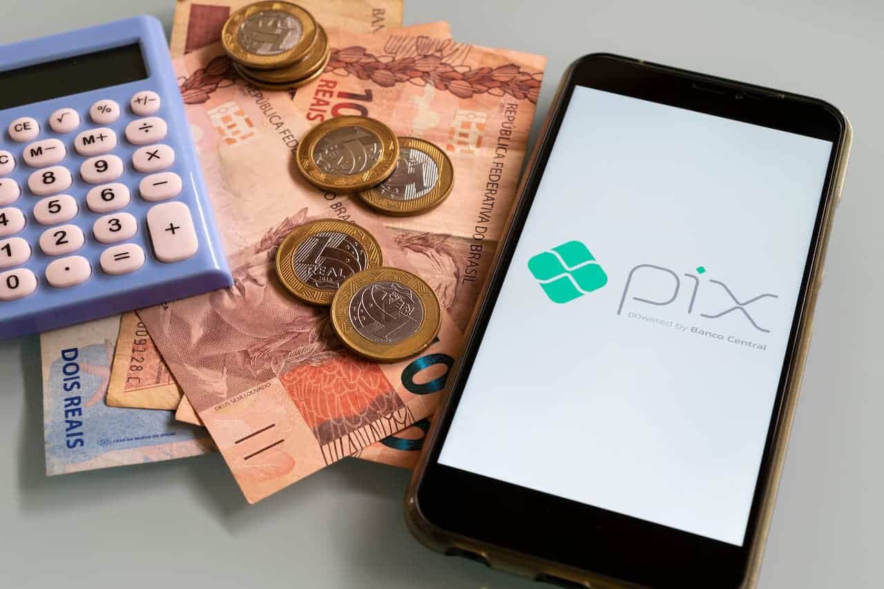Celular com logo do Pix, ao lado de modeas e notas de real e de uma calculadora