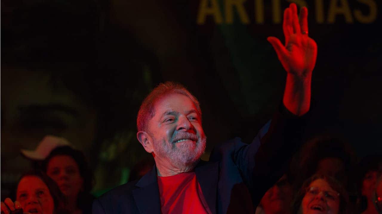 Foto do presidente Lula sorrindo com a mão para o alto