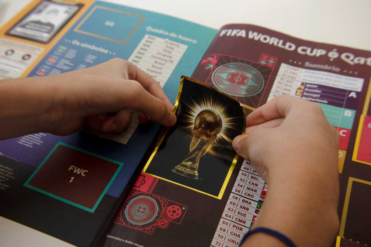 Mão colando figurinha em álbum da Copa do Mundo